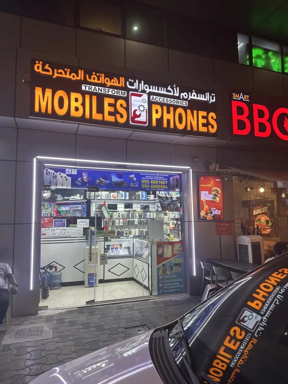 The same shopfront at night with the amber sign lit, next door to Smart BBQ