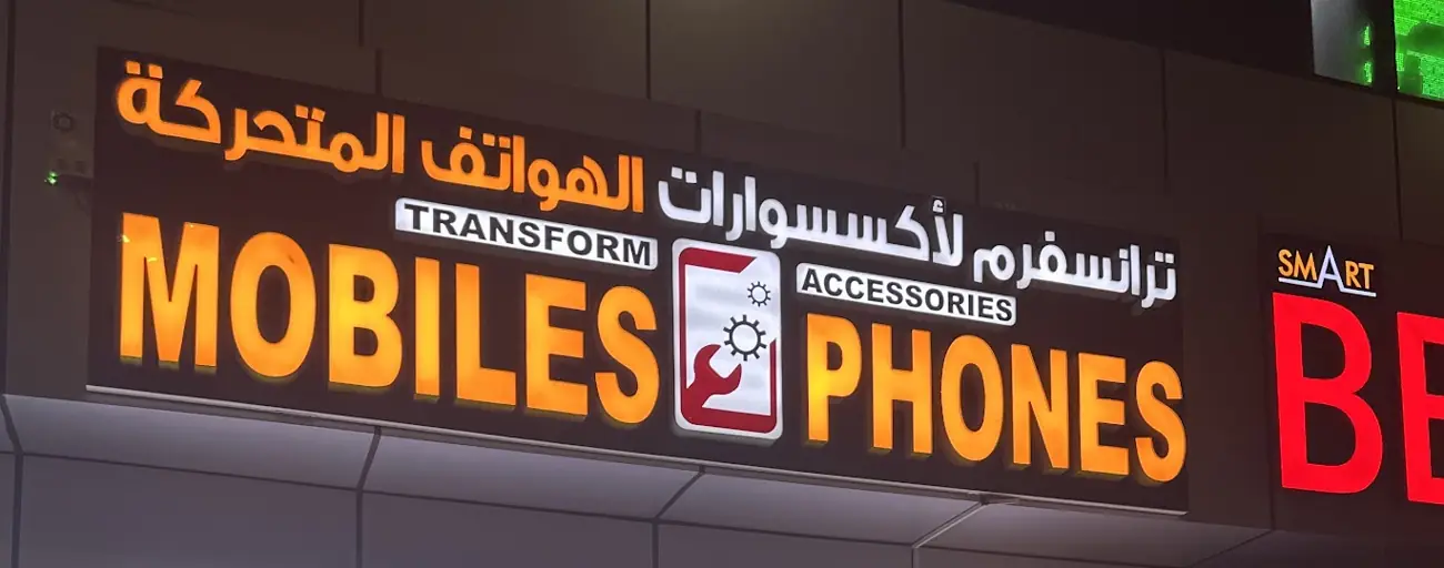 The lit Transform Mobiles sign at night, in English and Arabic